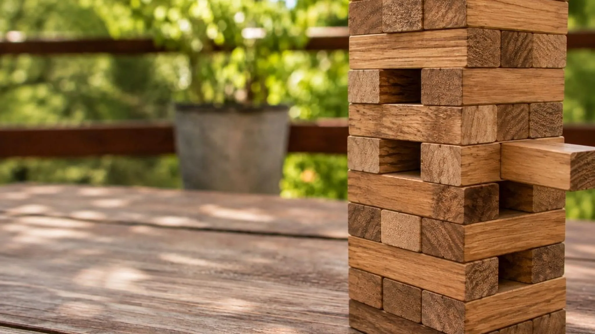A tower of wooden blocks part way through a game, one block pulled out, on a sunlit table