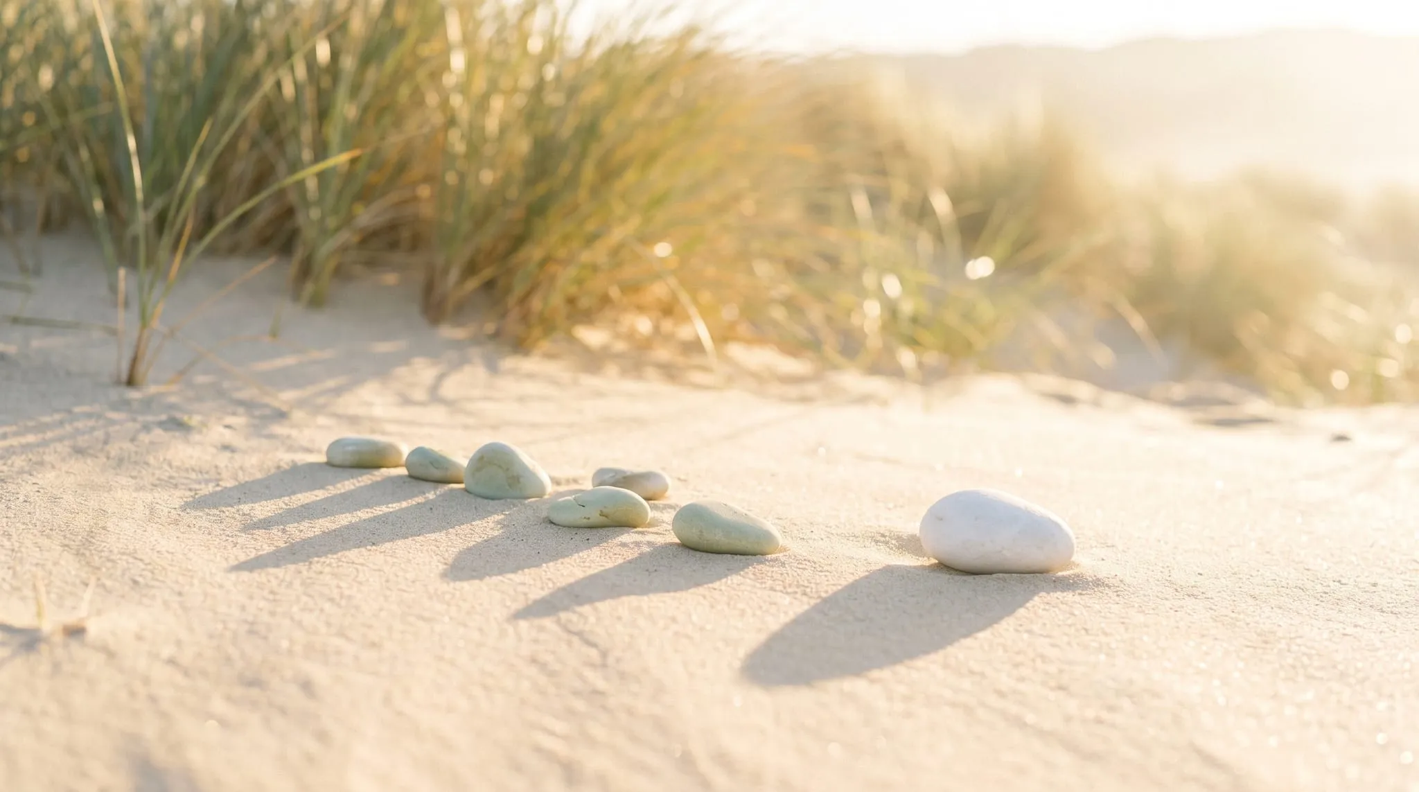 A loose row of pale pebbles on bright sand with one pebble set apart from the rest
